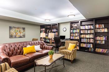 A living room with a brown leather couch, a chair, a coffee table, and a bookshelf filled with books.